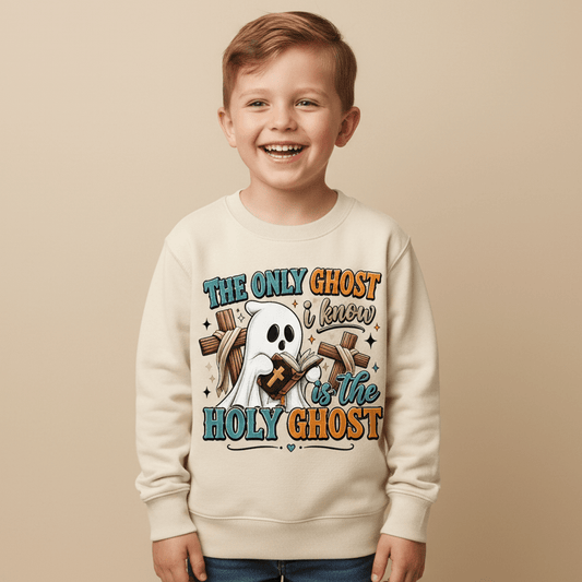 A smiling young boy wears the Toodleroos “The Only Ghost I Know Kids Sweatshirt – Holy Ghost Halloween Pullover,” featuring a cream color, a cartoon ghost holding a cross, and colorful lettering that reads “The only ghost I know is the Holy Ghost.” This faith-inspired Halloween sweatshirt for kids stands out against a neutral background.
