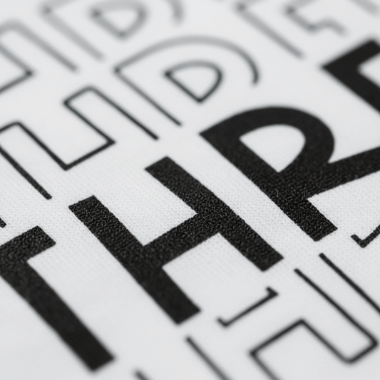 A close-up of bold black text spelling “THRE” on a white textured background, surrounded by abstract black line shapes and letters—an ideal inspiration for the Toodleroos Three Birthday Toddler Shirt – 3rd Birthday Tee, perfect for a gender-neutral birthday look.