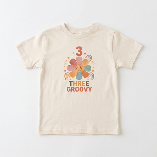 Celebrate your little one’s 3rd birthday in style with the Toodleroos 3rd Birthday Toddler Shirt – Three Groovy Retro Flower Tee, featuring a beige kids’ T-shirt decorated with a smiling flower, rainbows, stars, the number 3, and colorful “Three Groovy” retro-style lettering—perfect as a birthday shirt for toddlers or a fun retro flower tee for their special day.