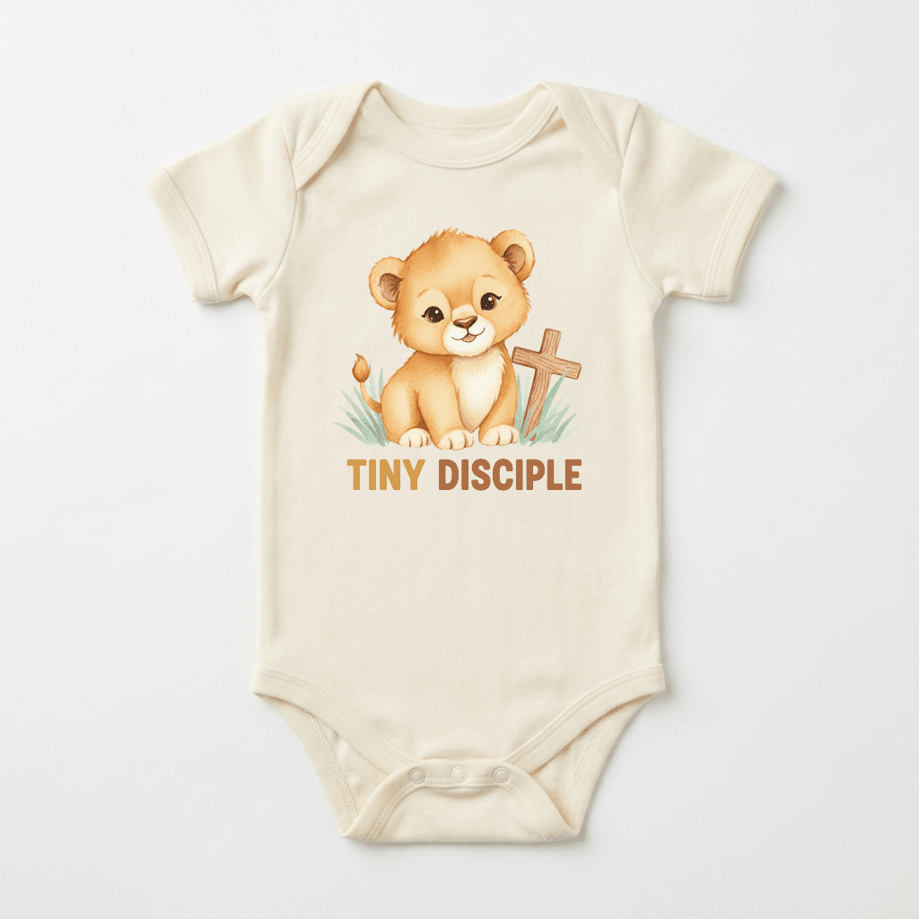 Dress your little one in the Tiny Disciple Baby Onesie – Christian Lion Design from Toodleroos, featuring a charming illustrated lion cub sitting on grass beside a wooden cross. The words “TINY DISCIPLE” are printed below in bold brown letters, making this cream baby onesie a perfect baptism gift for any child.