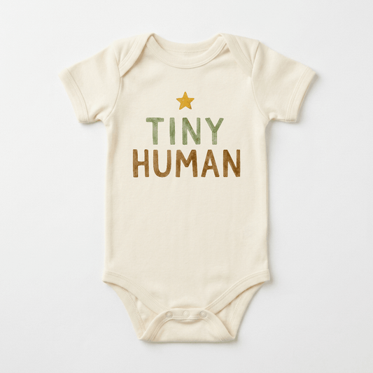 The Toodleroos Gender-Neutral Baby Onesie – Tiny Human Short-Sleeve Graphic Bodysuit showcases a cream-colored design with a yellow star and the phrase “TINY HUMAN” printed in green and brown lettering on the front, making it an ideal pick for fans of minimalist baby bodysuits and neutral baby clothing.