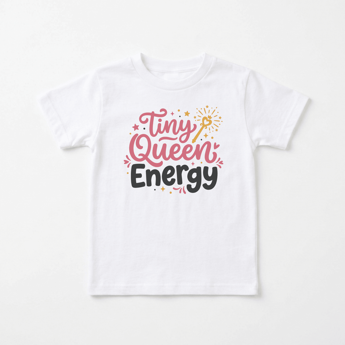 The Tiny Queen Energy Toddler Tee – Cute Girls Shirt by Toodleroos is a white toddler tee for girls, featuring colorful, playful “Tiny Queen Energy” text in pink and black letters surrounded by small stars and sparkles. This adorable Toodleroos shirt is laid flat on a light background.