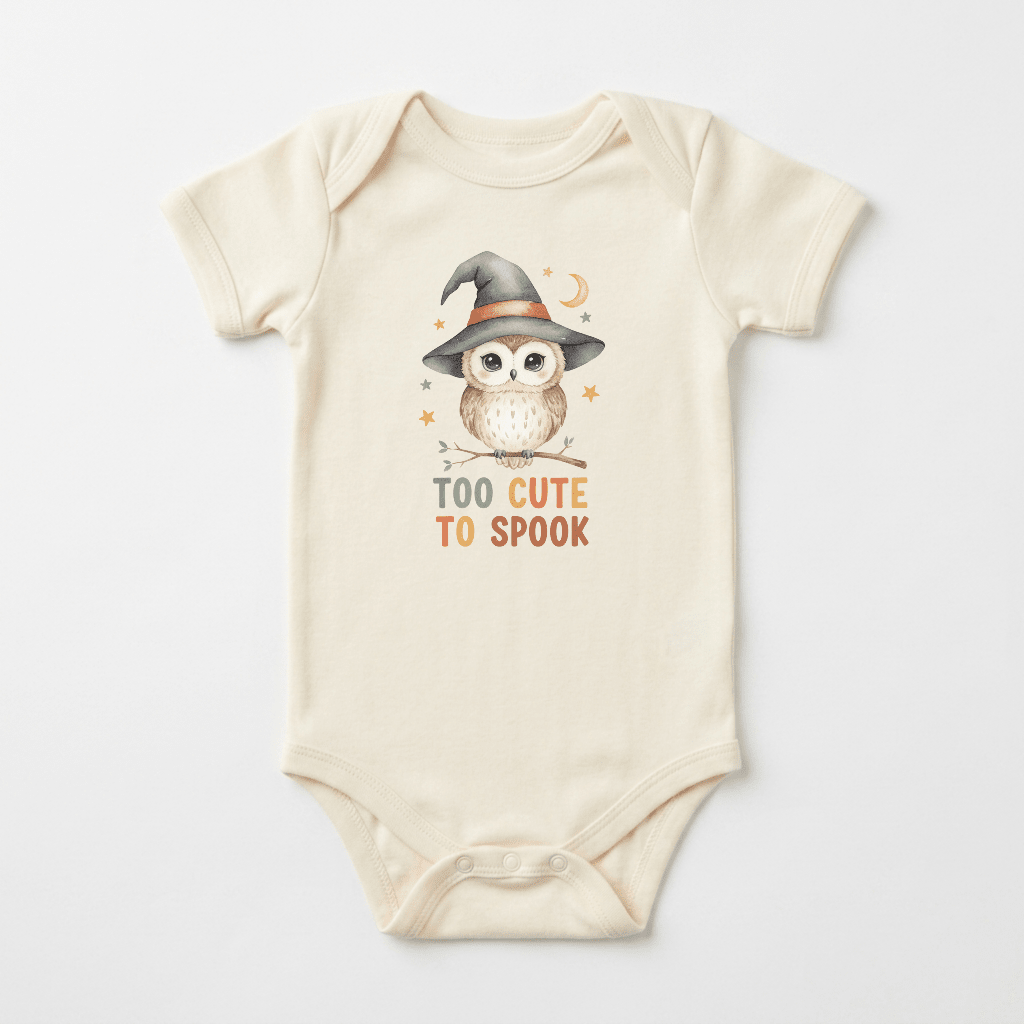 Dress your little one for their first Halloween with the Toodleroos Halloween Baby Onesie – Too Cute to Spook Owl Short-Sleeve Bodysuit, featuring a beige design with an adorable owl in a witch hat perched on a branch and “Too Cute To Spook” printed below—a charming choice for any baby who loves owls.