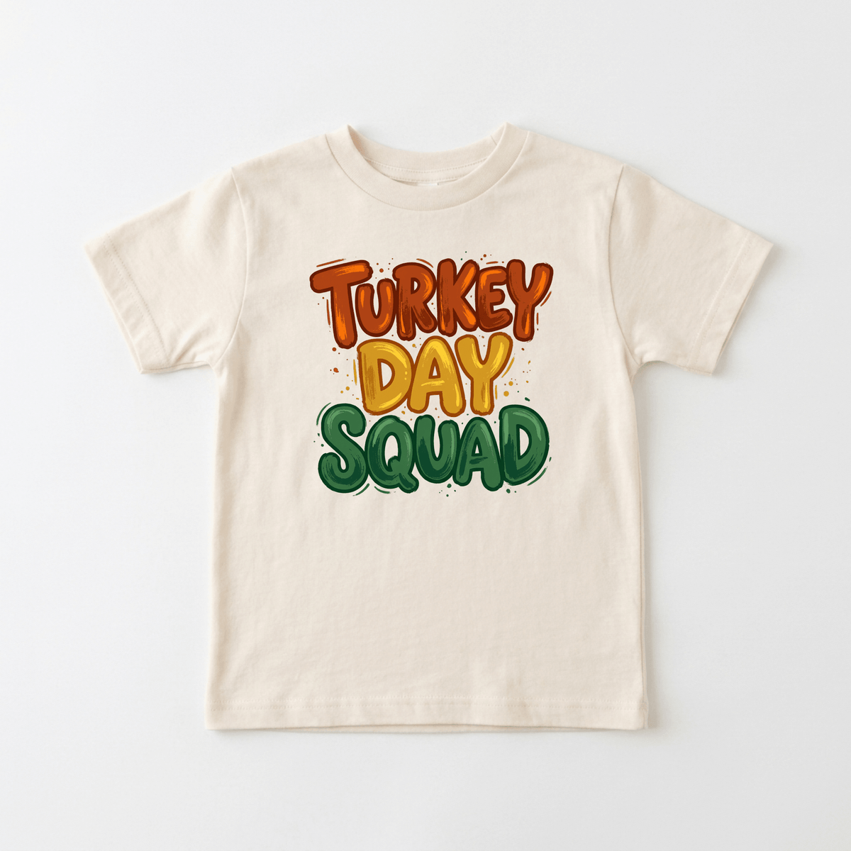 The Toodleroos Turkey Day Squad Toddler Tee – Thanksgiving Kids Shirt features the playful phrase “Turkey Day Squad” in bold orange, yellow, and green letters on a beige background, making it the perfect addition to your little one’s fall wardrobe.