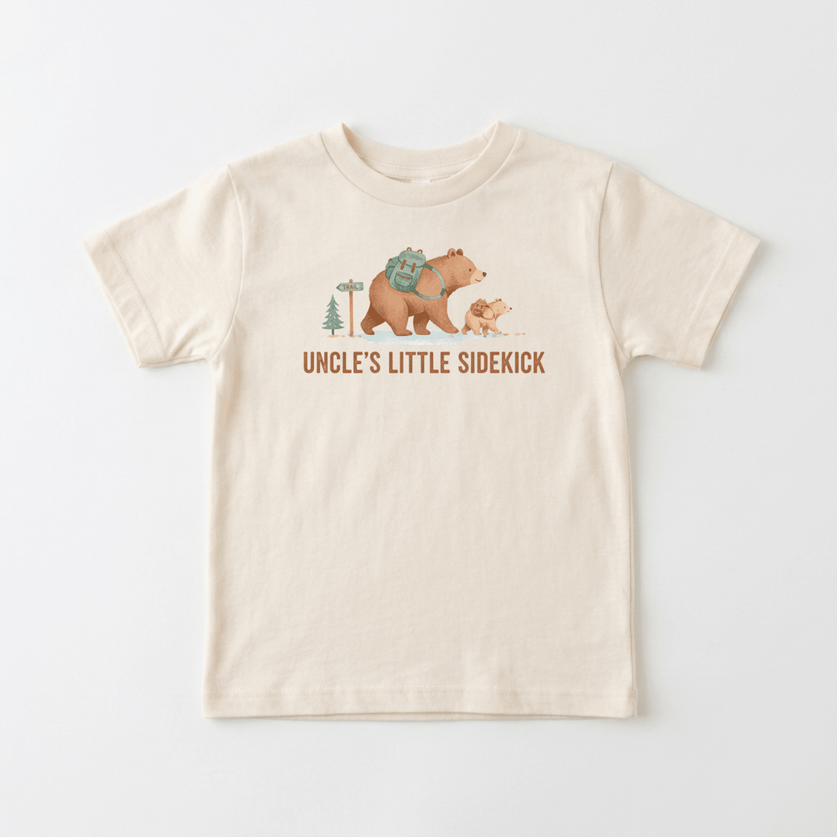 The Toodleroos Uncle’s Little Sidekick Toddler Shirt – Hiking Bear Tee is a beige t-shirt displaying an illustration of a large bear with a backpack and a small bear cub by a pine tree and sign, with “UNCLE’S LITTLE SIDEKICK” printed below—making it the perfect uncle toddler shirt or hiking bear toddler tee for outdoor adventures together.