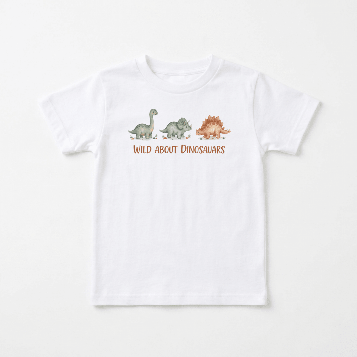 The Toodleroos Wild About Dinosaurs Toddler Shirt – Watercolor Dino Tee features a white background with playful, watercolor illustrations of three dinosaurs in green, gray, and brown above the phrase “WILD ABOUT DINOSAURS” in bold orange letters. This cheerful dinosaur toddler shirt is perfect for adventurous little ones and makes an ideal toddler graphic tee for any dino-loving kid.