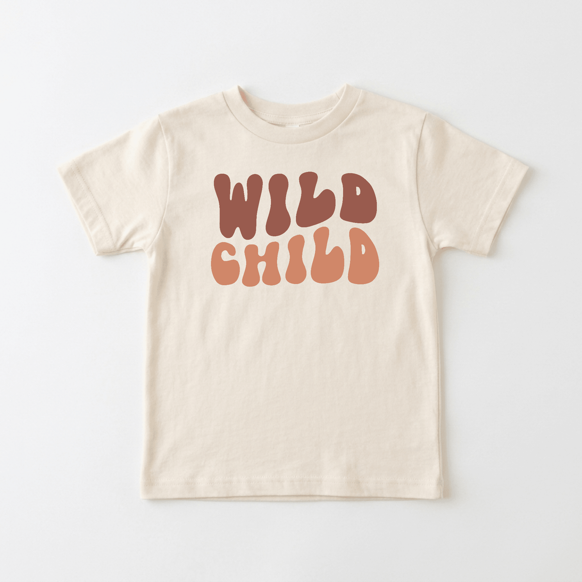 Showcasing the Wild Child Kids Shirt – Boho Retro Tee by Toodleroos, this beige t-shirt features “WILD CHILD” printed boldly on the front in large, playful brown and peach retro-style letters. Perfect for fans of boho kids shirts, this Toodleroos tee adds a fun, vintage-inspired flair to any child’s wardrobe. The shirt is displayed flat against a white background.