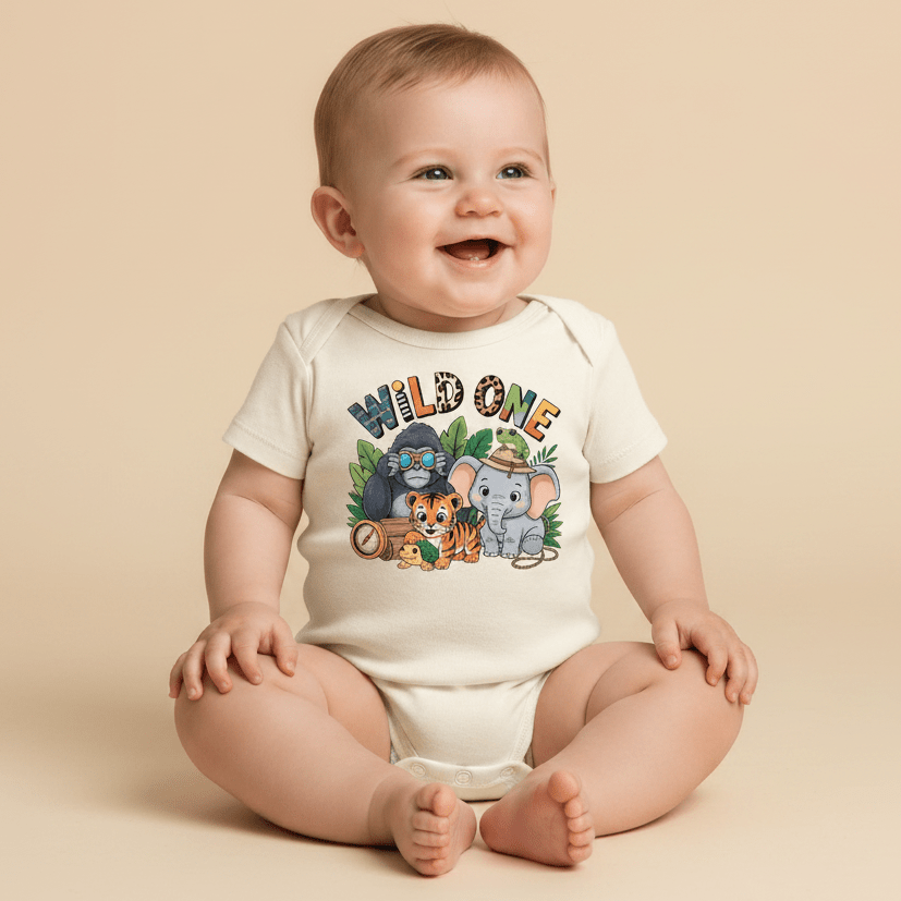 A happy baby sits on the floor wearing the Toodleroos Wild One 1st Birthday Baby Onesie – Jungle Safari Bodysuit, featuring cartoon animals like a lion, tiger, elephant, and koala. Surrounded by green leaves on a beige background, this adorable outfit is perfect for a safari-themed first birthday.