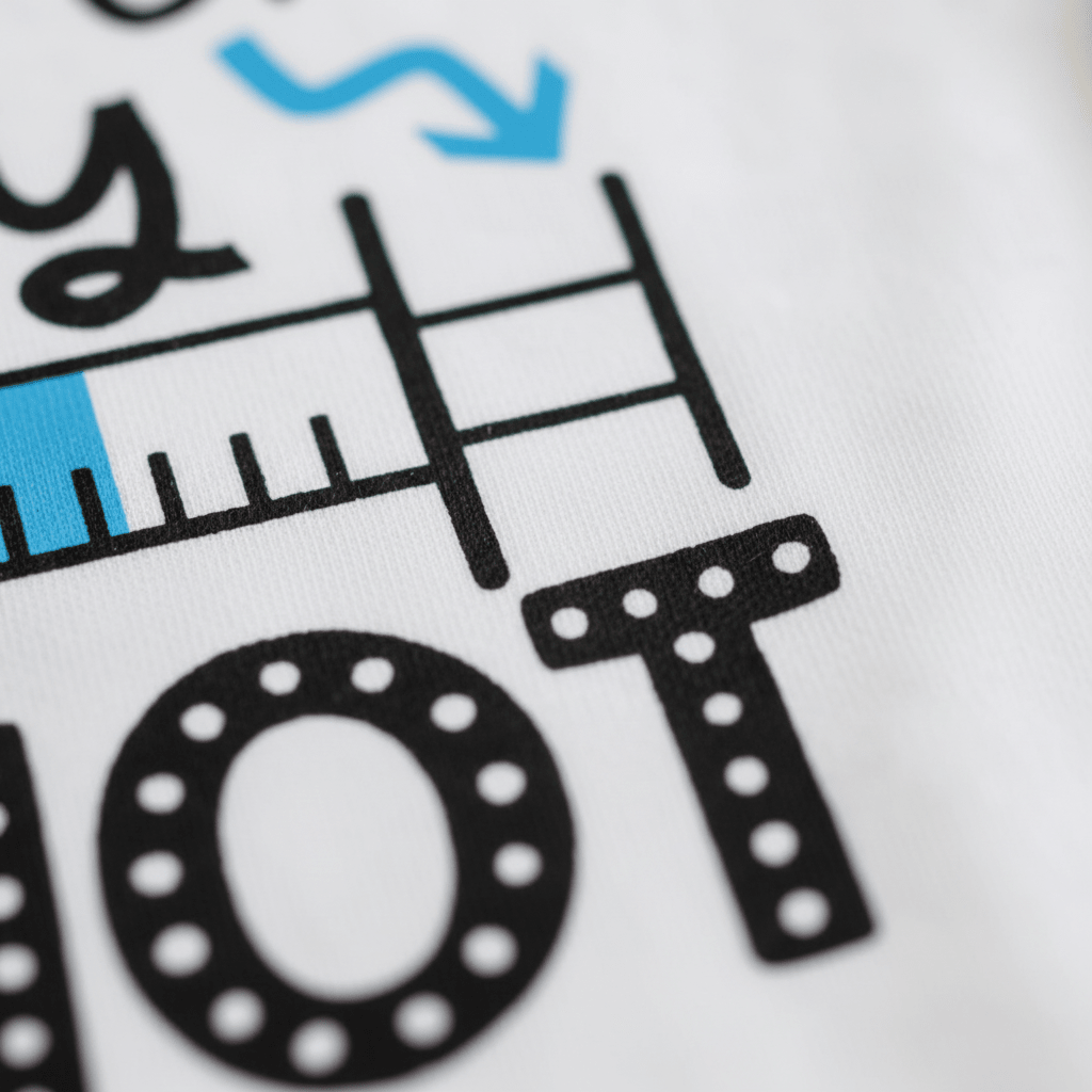 Close-up of the Worth Every Shot Baby Onesie by Toodleroos, featuring a printed design with a ruler, blue arrow, and bold black lettering with white dots on a white background—perfect for a baby announcement outfit or as a thoughtful IVF journey gift.