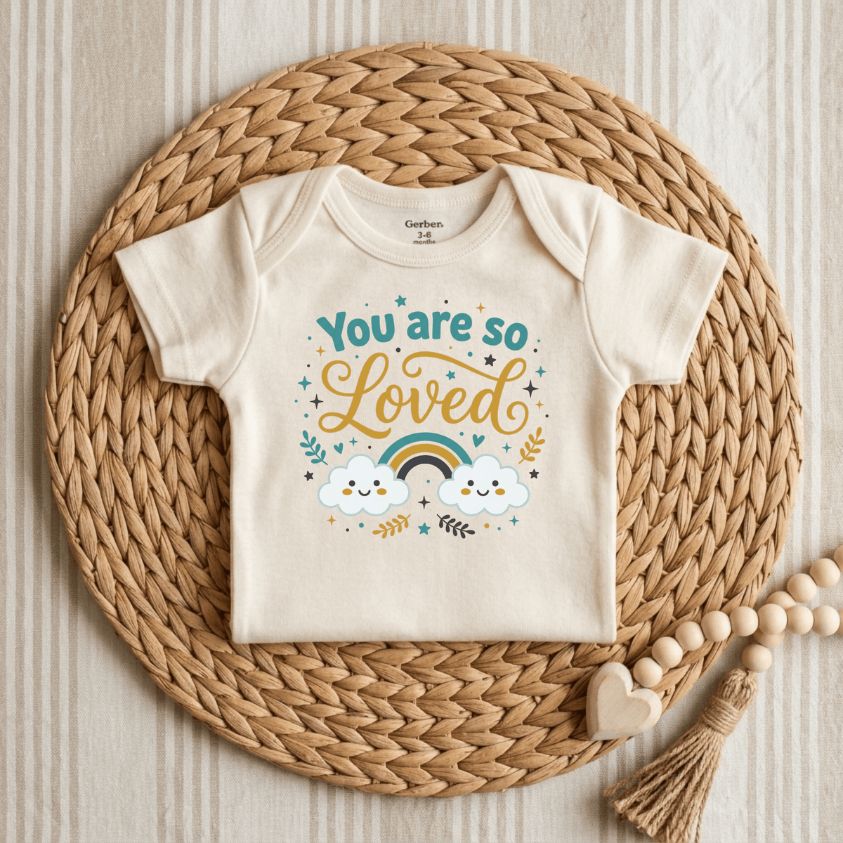 Welcome any little one with love thanks to the You Are So Loved Onesie – Cute Baby Rainbow Bodysuit by Toodleroos. This unisex baby onesie features a heartwarming “You are so loved” message, charming rainbow, clouds, and stars illustration. Pictured on a woven mat with wooden beads and a heart, it’s the perfect gender-neutral baby gift for new arrivals.