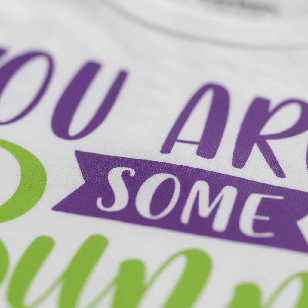 Close-up of a white fabric unisex baby onesie from Toodleroos, featuring the “You Are Some Bunny Special” design with purple, white, and green lettering printed on the material—an adorable spring baby shower gift.