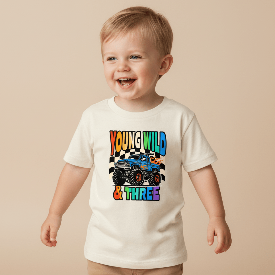 A smiling young boy wears the Toodleroos Young Wild & Three Toddler Shirt – Monster Truck 3rd Birthday Tee, featuring a cartoon monster truck and colorful “Young Wild & Three” text—the perfect shirt for any toddler who loves monster trucks on their 3rd birthday.